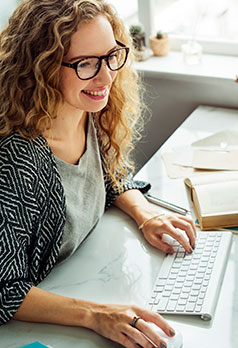 woman with curly hair and glasses typing on computer keyboard